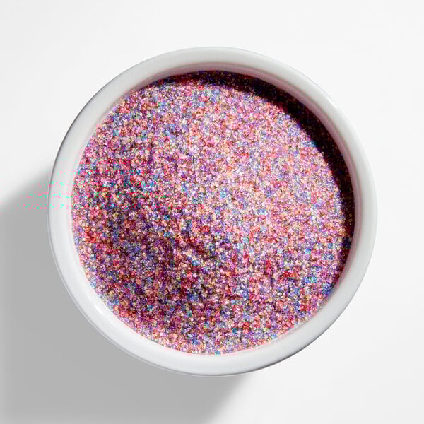 A white bowl filled with fine rainbow-colored sanding sugar.