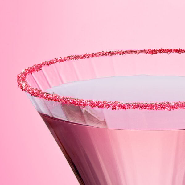 A close-up of a cocktail glass rimmed with fine pink sanding sugar.