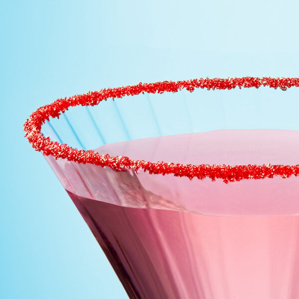 A pink cocktail with Adourne red sanding sugar on top on a table in a cocktail bar.