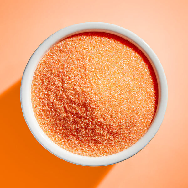 A white bowl filled with fine orange sanding sugar.