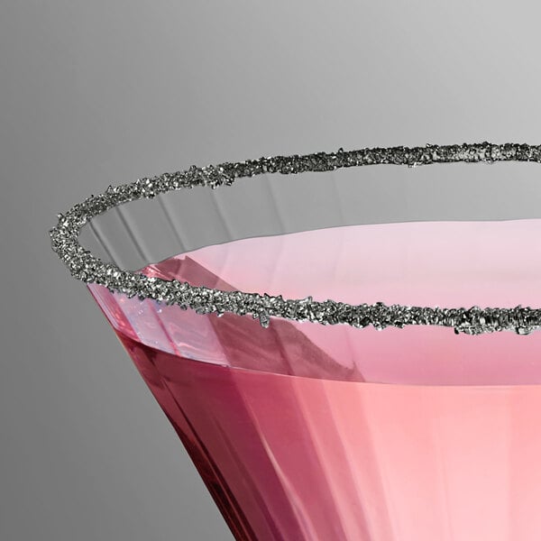 A close-up of a cocktail glass rimmed with fine black sanding sugar and filled with a pink beverage.