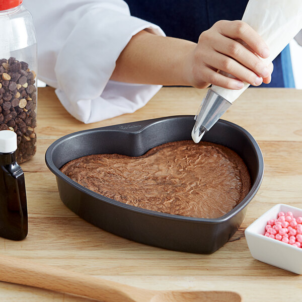 Baker frosting a heart shaped chocolate cake.