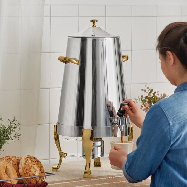 A woman pouring coffee from a Choice stainless steel coffee chafer urn with gold accents.