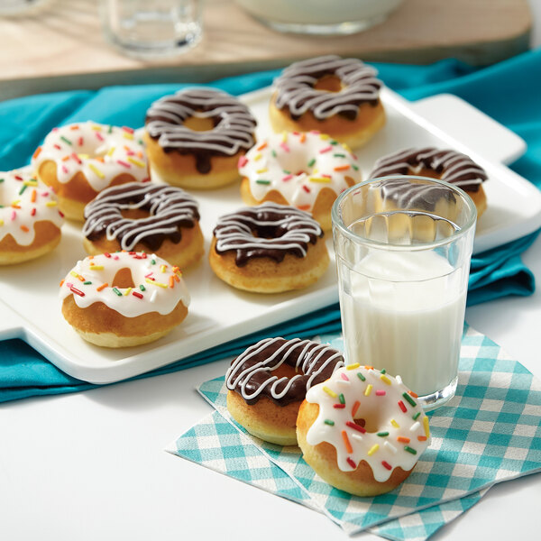 A plate with Wilton medium donuts with white frosting and sprinkles and a glass of milk.