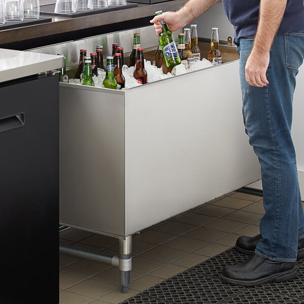 A man standing next to a Regency stainless steel beer box full of bottles of beer.