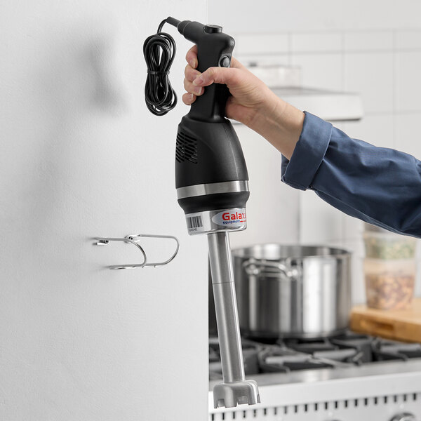 A black and silver 9-inch light-duty variable speed immersion blender being held in a kitchen setting.