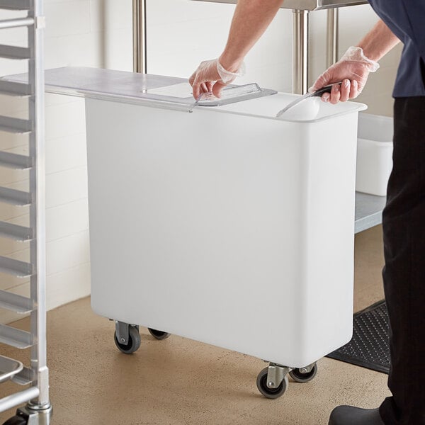 A person putting food into a white Carlisle ingredient container with a sliding lid.