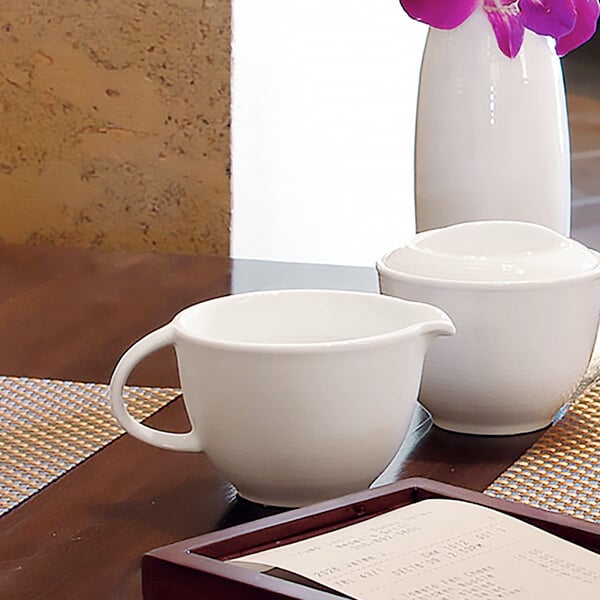 A white table with a white cup and Front of the House white porcelain creamer on it.