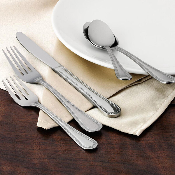 A white plate with a Walco Accolade stainless steel teaspoon and fork.