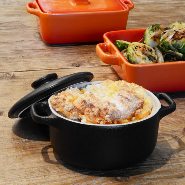 A black Front of the House round stoneware ovenware dish with a lid containing food.