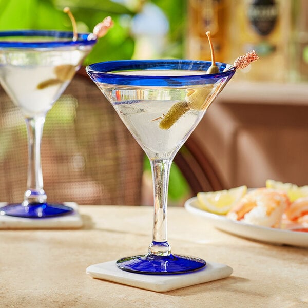 Two Acopa Tropic martini glasses with blue rims and bases filled with blue liquid on a table