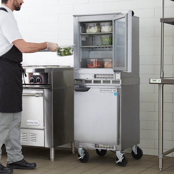 A man in a black apron standing in a professional kitchen with a Beverage-Air undercounter refrigerator on a counter.