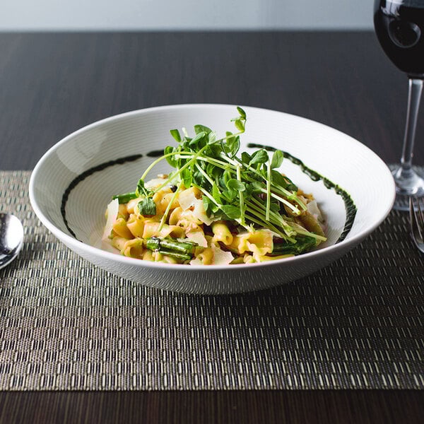 A white porcelain bowl filled with pasta with a glass of wine.