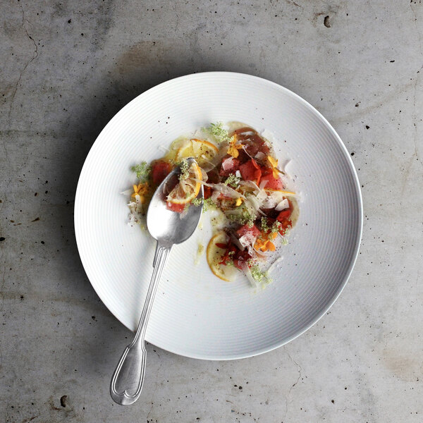 A Front of the House white porcelain plate with food and a spoon on it.