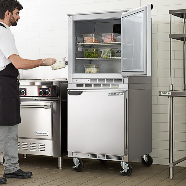 A man in a black apron putting food into a Beverage-Air undercounter refrigerator.