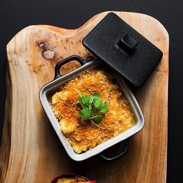 A black square stoneware casserole dish with a lid on a wood cutting board.