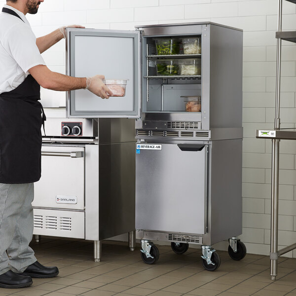 A man in an apron opening a white Beverage-Air undercounter refrigerator with left hinged doors.