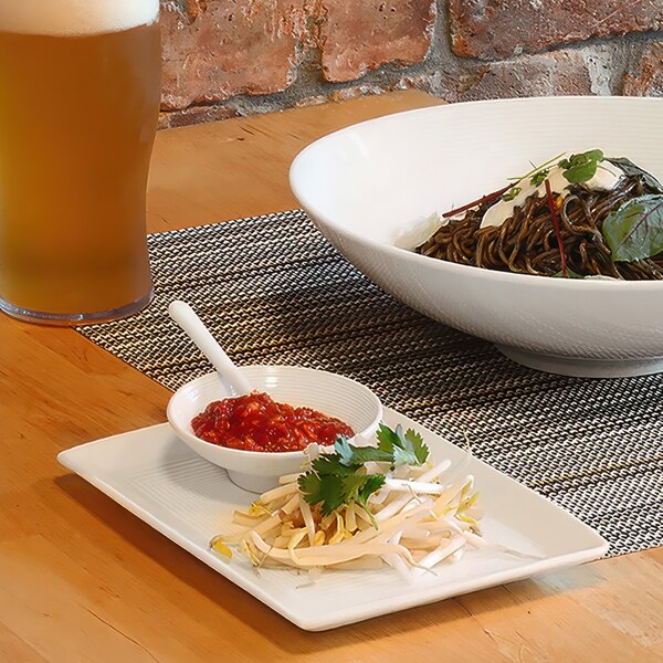 A rectangular white porcelain plate with food and a glass of beer on a table.