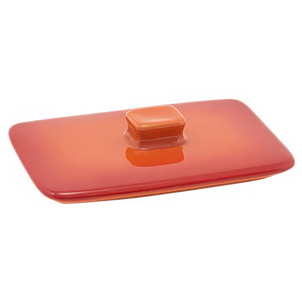 A rectangular orange stoneware lid with a square object on it.