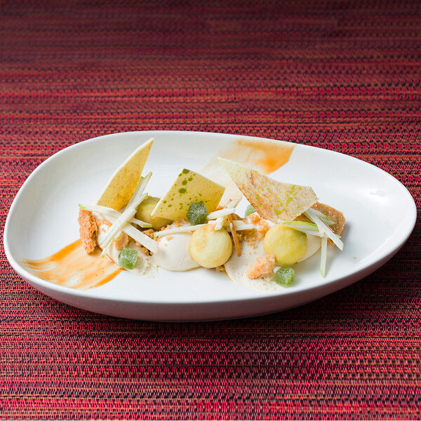 A vanilla bean porcelain oval plate with food on it on a red table.