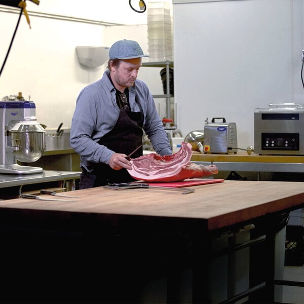 A man cutting meat on a Vollrath cutting board.
