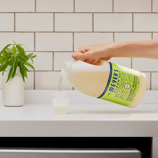 A person pouring Mrs. Meyer's Lemon Verbena Laundry Detergent into a plastic container.