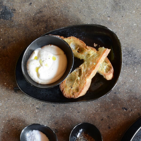 A black and white porcelain oval plate with food and a bowl of dip on it.