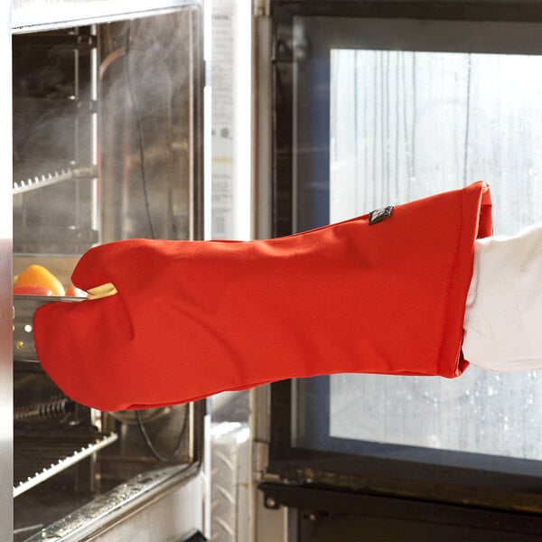 A person wearing a San Jamar oven mitt holding a pan.