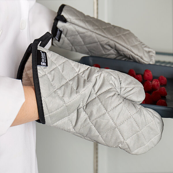 A person wearing San Jamar oven mitts holding a tray of raspberries.