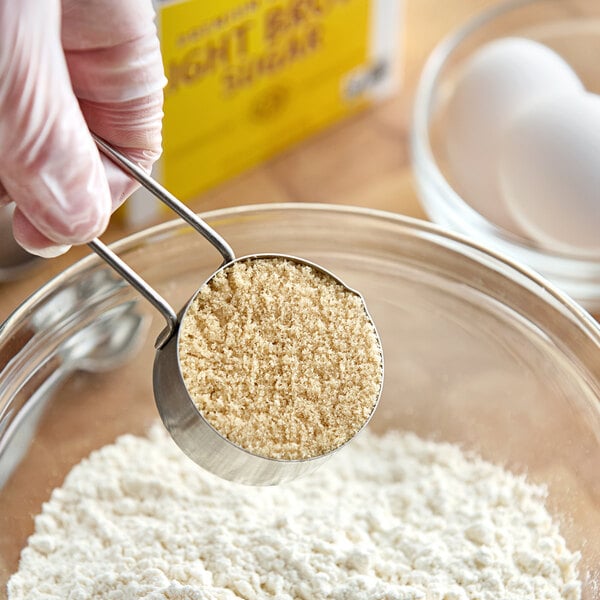 A person holding a measuring cup with a brown powder pouring into a bowl.