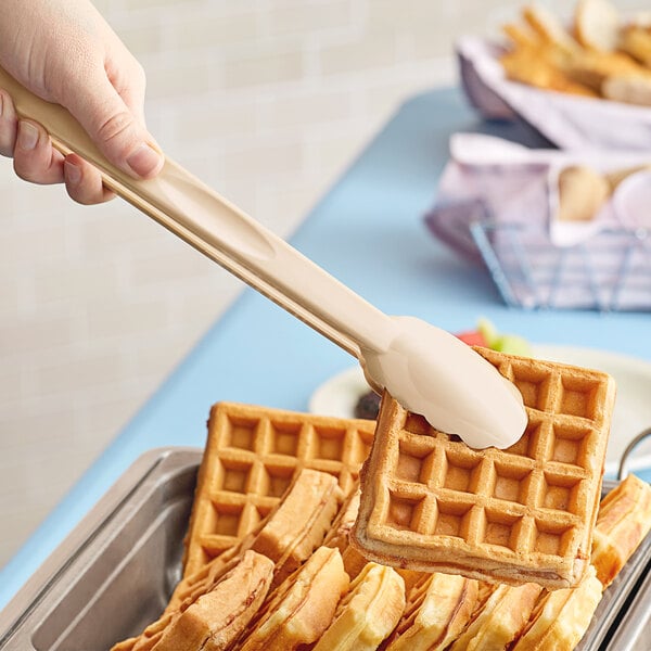 A person using Cambro beige plastic tongs to serve waffles at a hotel buffet.
