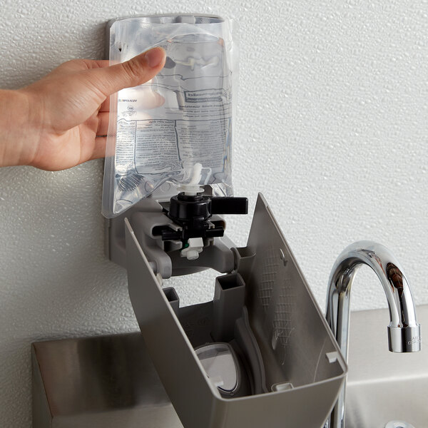 A hand using a Rubbermaid metallic gray manual spray soap dispenser to fill a plastic bag with liquid soap.