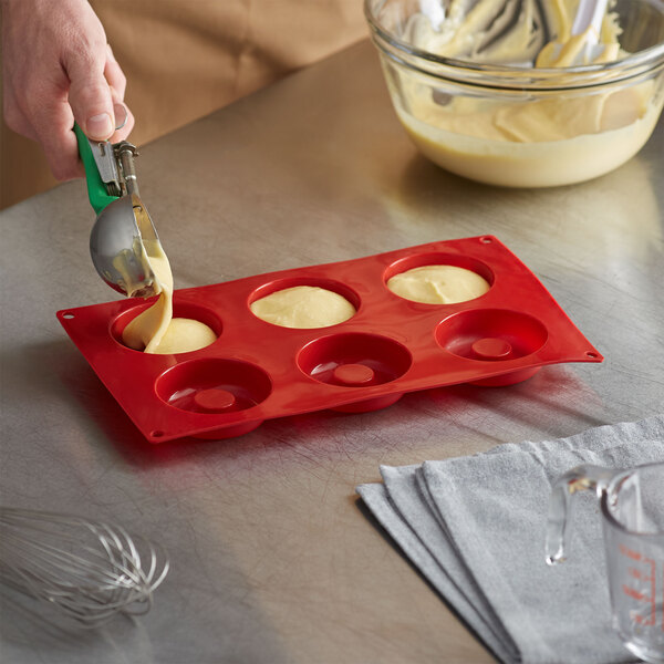 A person pouring batter into a Thunder Group red silicone savarin mold with 6 compartments.