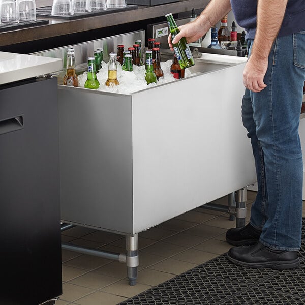 A man standing at a counter with a Regency stainless steel beer cooler and putting bottles in it.