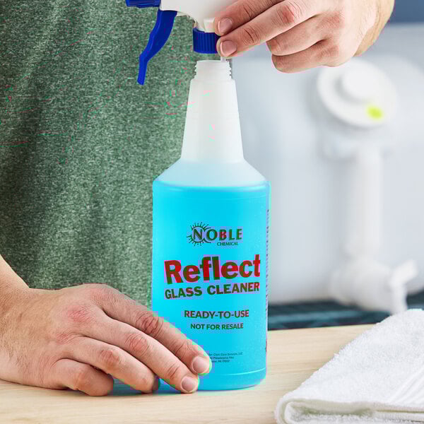 A hand holding a blue 32 oz. Noble Chemical Reflect spray bottle.