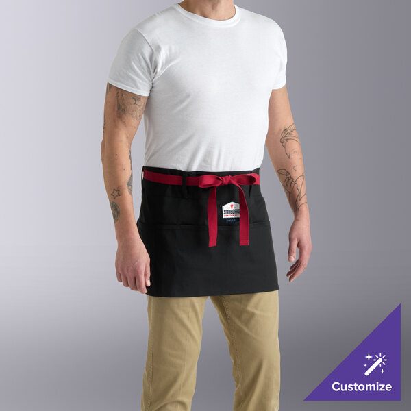 A black waist apron with red webbing and three pockets, worn by a person over khaki pants and a white shirt.