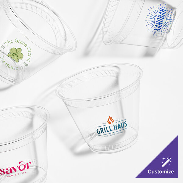 A group of clear Fabri-Kal customizable plastic cups with a green logo on one cup.