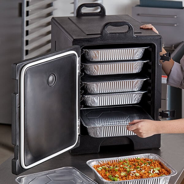 A woman using a Choice black front loading food pan carrier to transport trays of rice and vegetables.