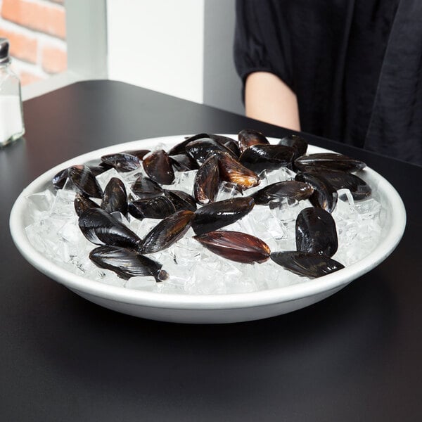 An American Metalcraft aluminum seafood tray holding a bowl of mussels on ice on a black table.