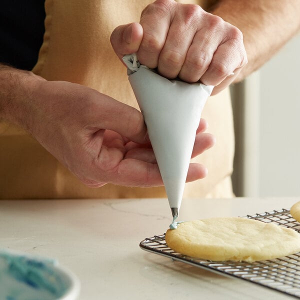 A person using an Ateco parchment pastry bag to frost a cookie.