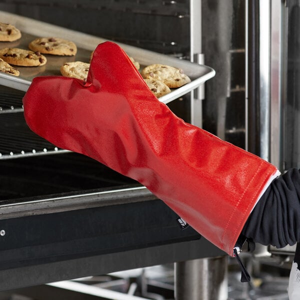A person wearing red San Jamar EZ-KLEEN oven mitts removes cookies from a tray.