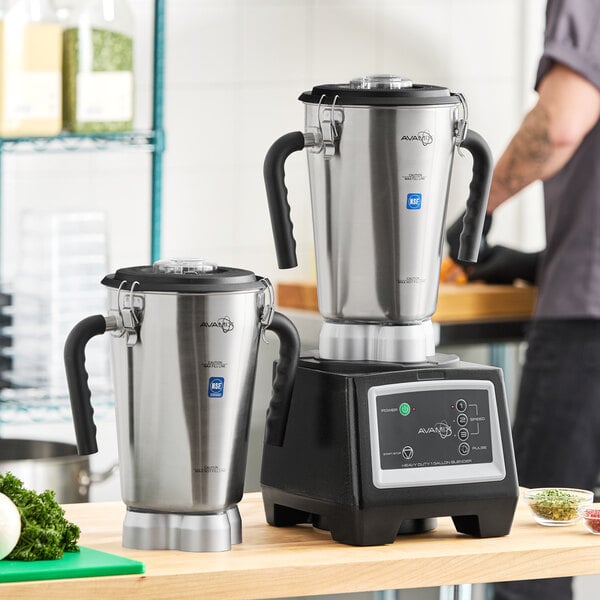 A heavy duty commercial food blender with a stainless steel base and two large stainless steel jars.