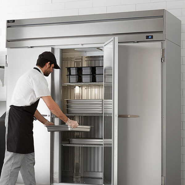 A man wearing a black apron and gloves opening a Beverage-Air Horizon Series glass door refrigerator.