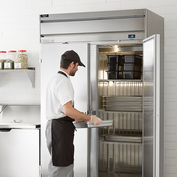 A man in a uniform and gloves opening the stainless steel door of a Beverage-Air reach-in refrigerator.