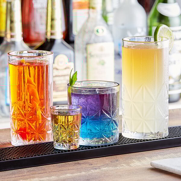 A table in a cocktail bar with a group of Acopa Gardenia highball glasses filled with different colored liquid.