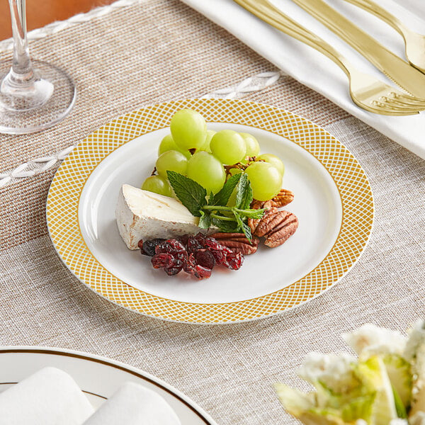 A Visions plastic plate with a gold lattice design holding cheese, grapes, and a green leaf.