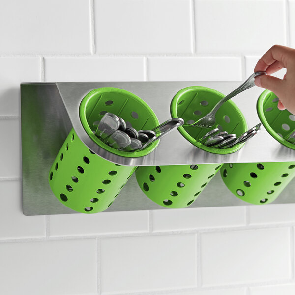 A hand holding a spoon in a lime green Steril-Sil flatware holder.