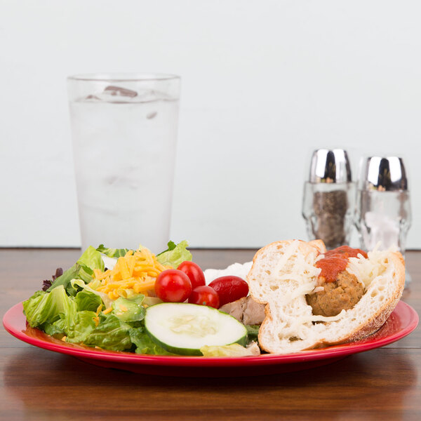 A Carlisle red melamine plate with a sandwich and salad on it.