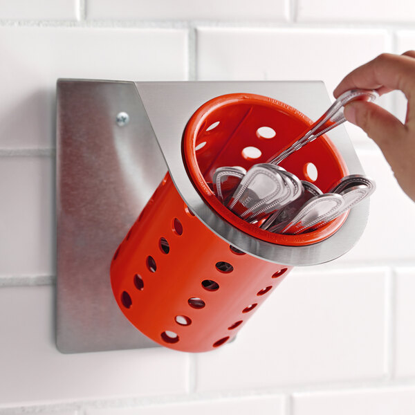 A hand holding a spoon in a red Steril-Sil flatware container.