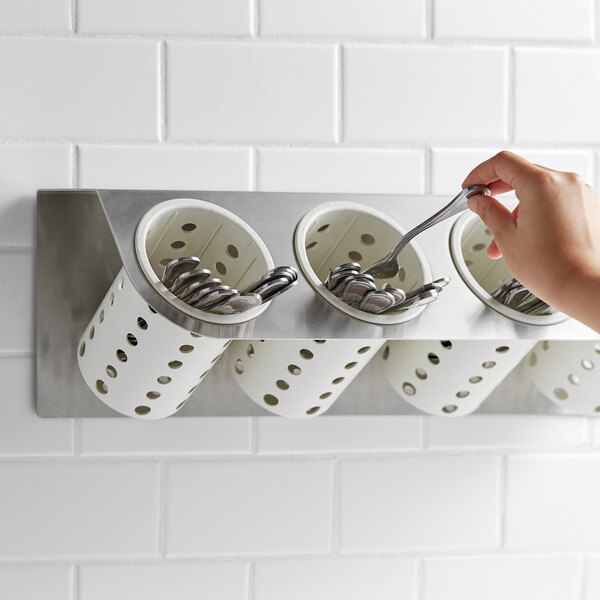 A hand holding a spoon in a Steril-Sil flatware rack with white cylinders.